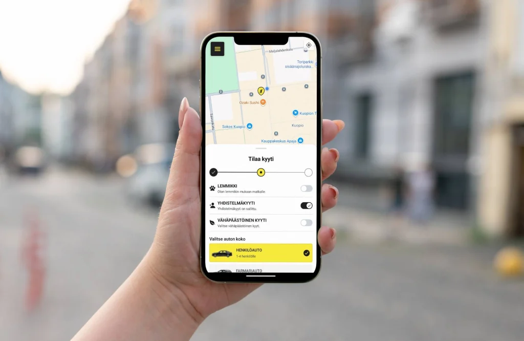 Taksi1 mobiilisovellus matkapuhelimen näytöllä ja ihmisen kädessä.