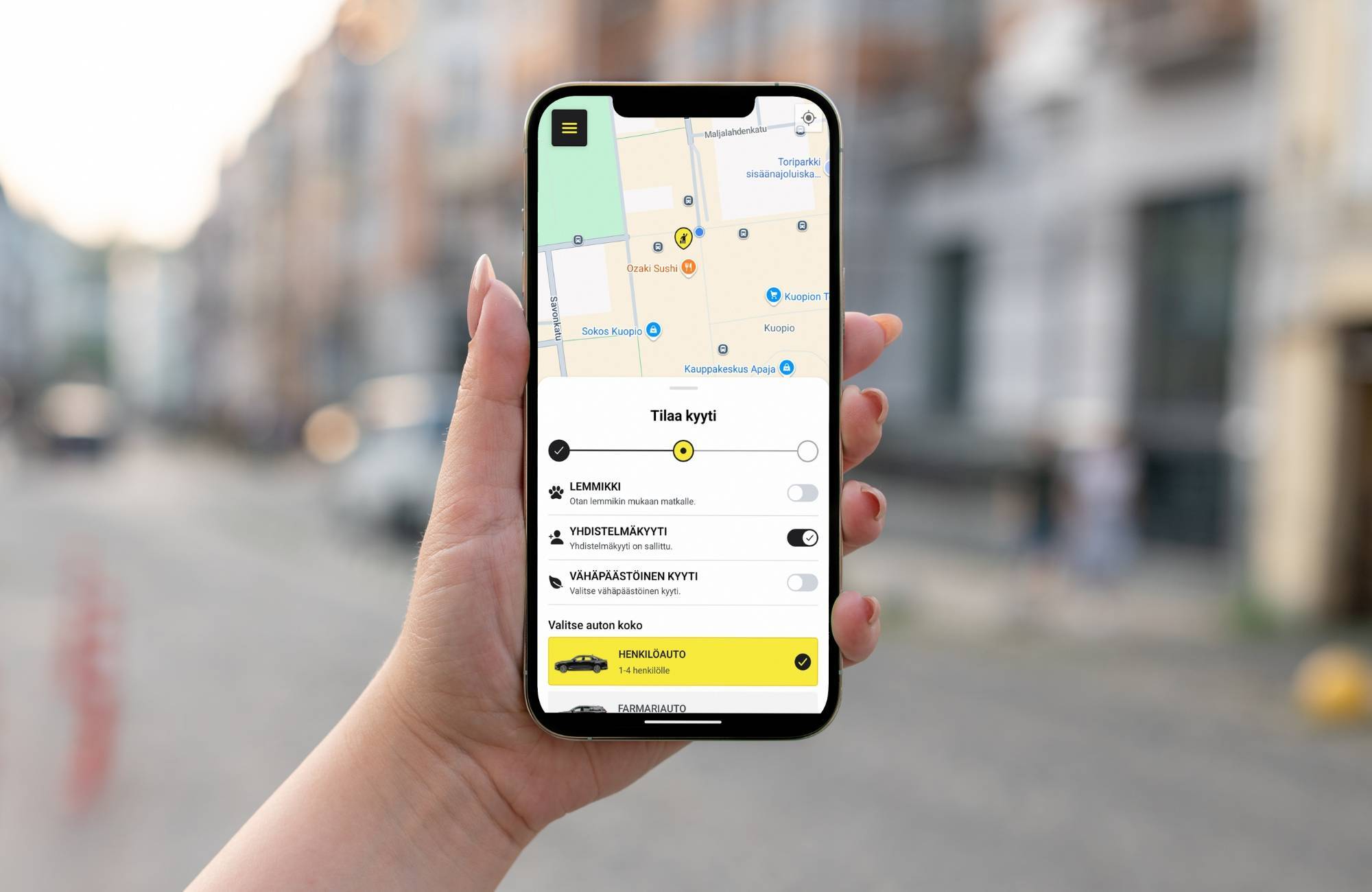 Taksi1 mobiilisovellus matkapuhelimen näytöllä ja ihmisen kädessä.